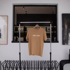 Beige t-shirt with 'HEY YOU!' text hanging in a modern interior setting.