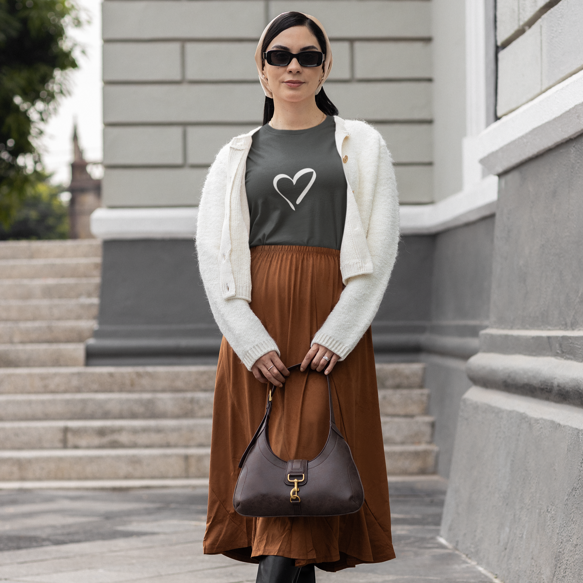Woman in a brown skirt and white cardigan standing on steps with a building in the background