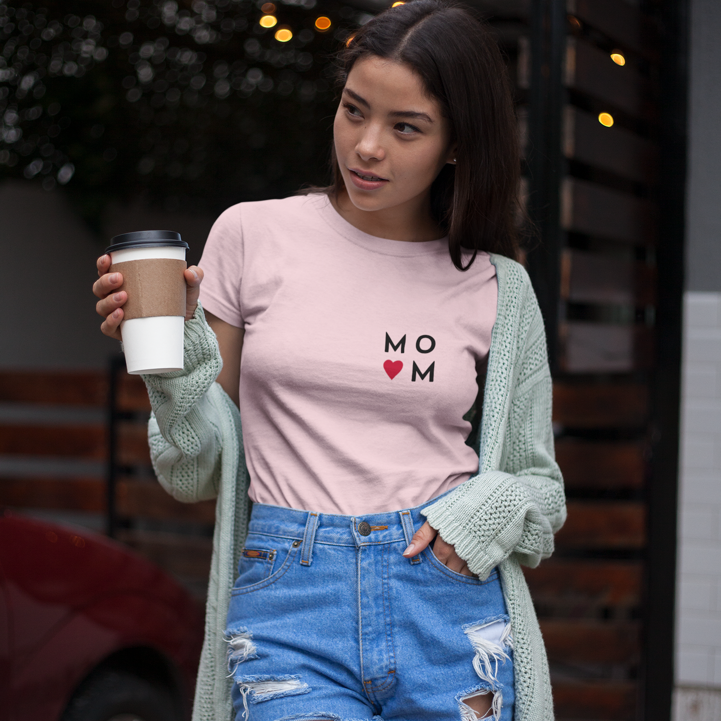 Woman wearing a pink t-shirt with 'MO MOM' text and holding a coffee cup outdoors.
