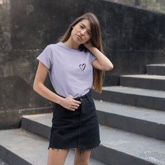 Woman wearing a light purple t-shirt with a heart design and a black skirt standing on stone steps.
