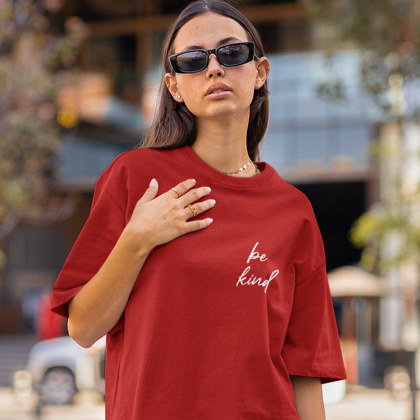 Woman wearing a red t-shirt with 'be kind' text on a street background