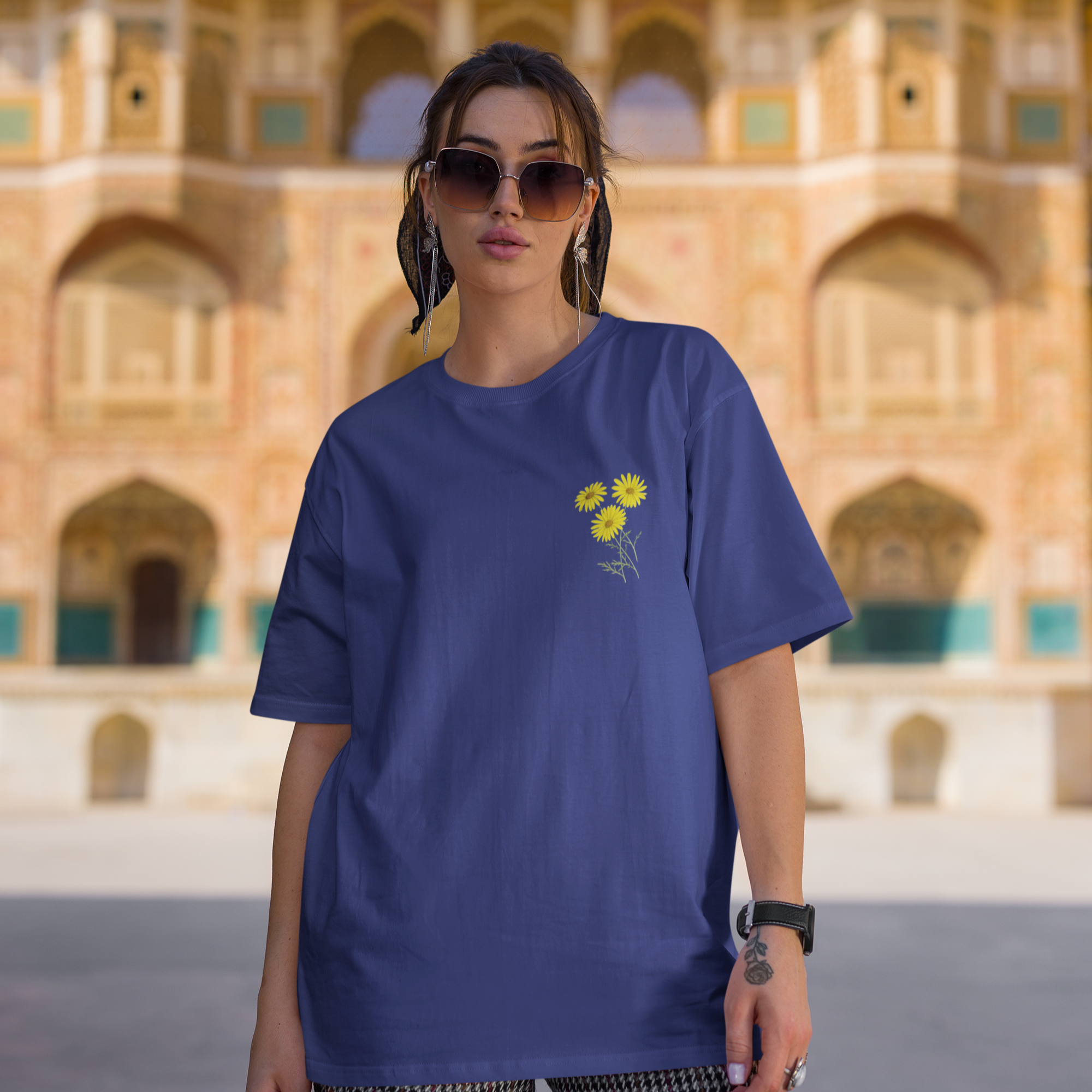 Person wearing a blue t-shirt with a yellow flower design in front of an architectural building.