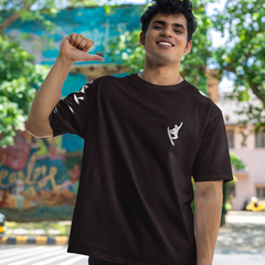 Person wearing a black t-shirt with a logo, standing outdoors with trees and buildings in the background.