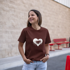 Woman wearing a brown t-shirt with a heart design, standing outdoors near a building.