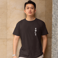 Man wearing a black t-shirt with a logo against a textured wall.