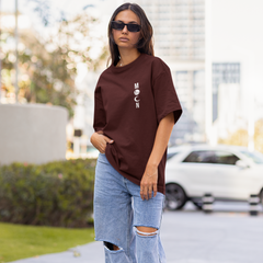 Woman wearing a brown t-shirt and ripped jeans standing on a sidewalk with blurred background