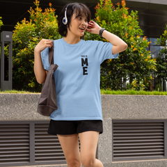 Person wearing a light blue t-shirt with text, black shorts, and black boots, standing outdoors.