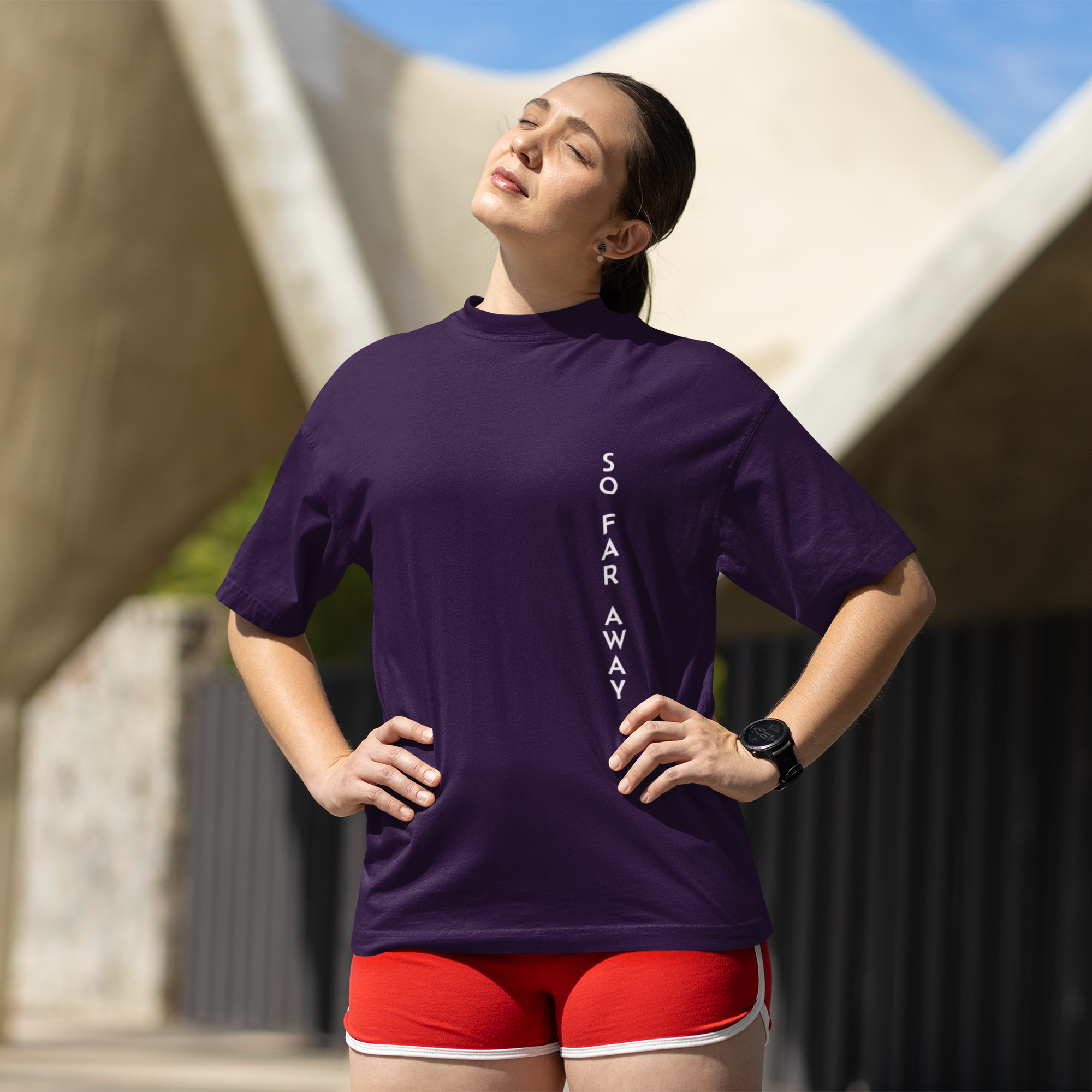 Woman wearing a purple athletic shirt with text, standing outdoors under a modern architectural structure.