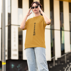 Person wearing a mustard yellow t-shirt and light blue jeans standing in front of a modern building.