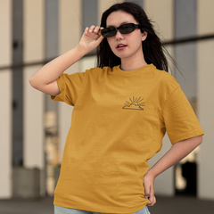 Woman wearing a mustard yellow t-shirt with a logo, standing outdoors.
