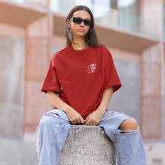 Person wearing a red t-shirt and ripped jeans sitting on a concrete block outdoors.