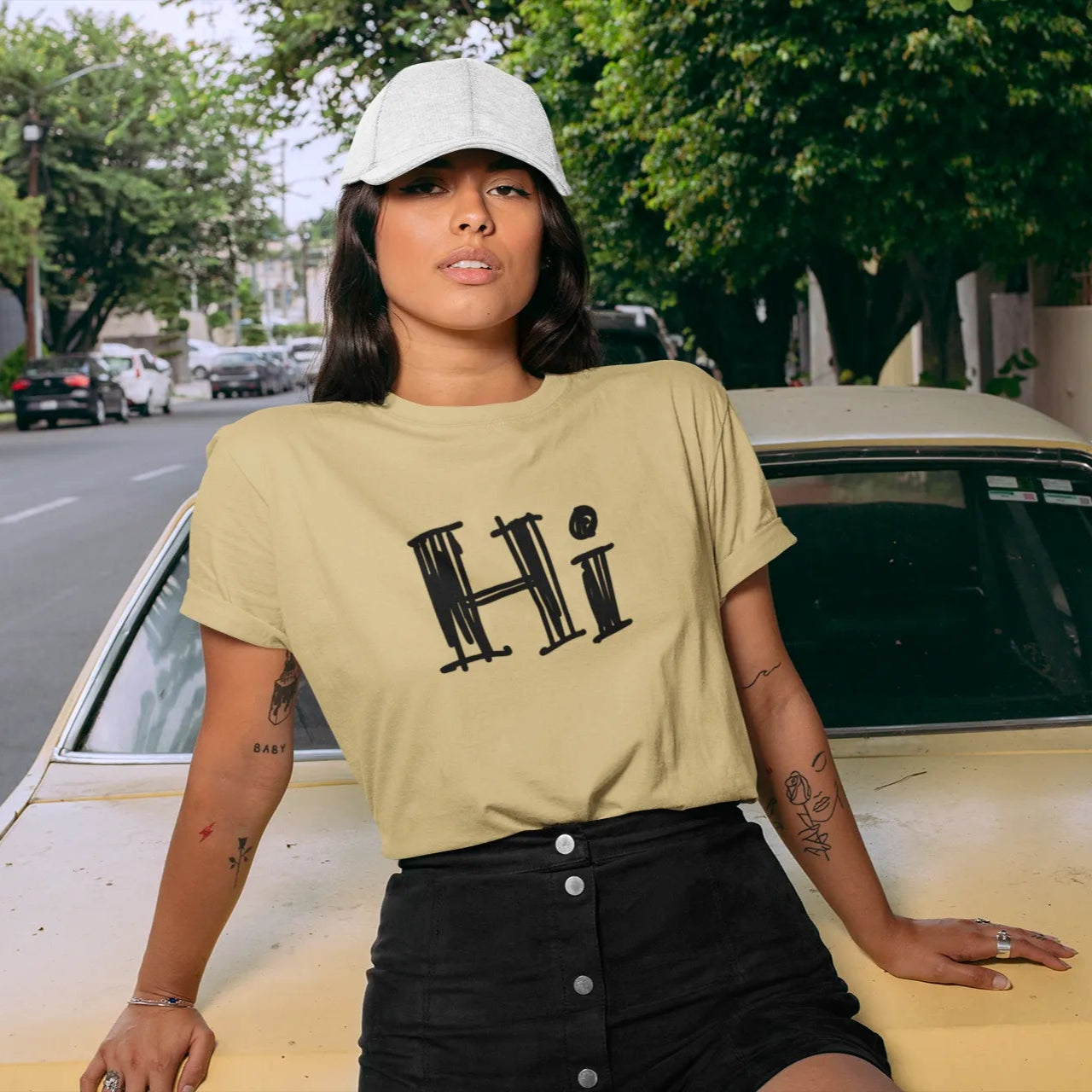Woman wearing a beige t-shirt with 'Hi' printed on it, standing next to a yellow car.