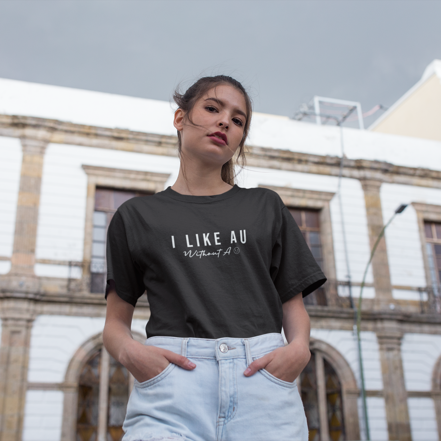 Woman wearing a black t-shirt with text, standing in front of a building.