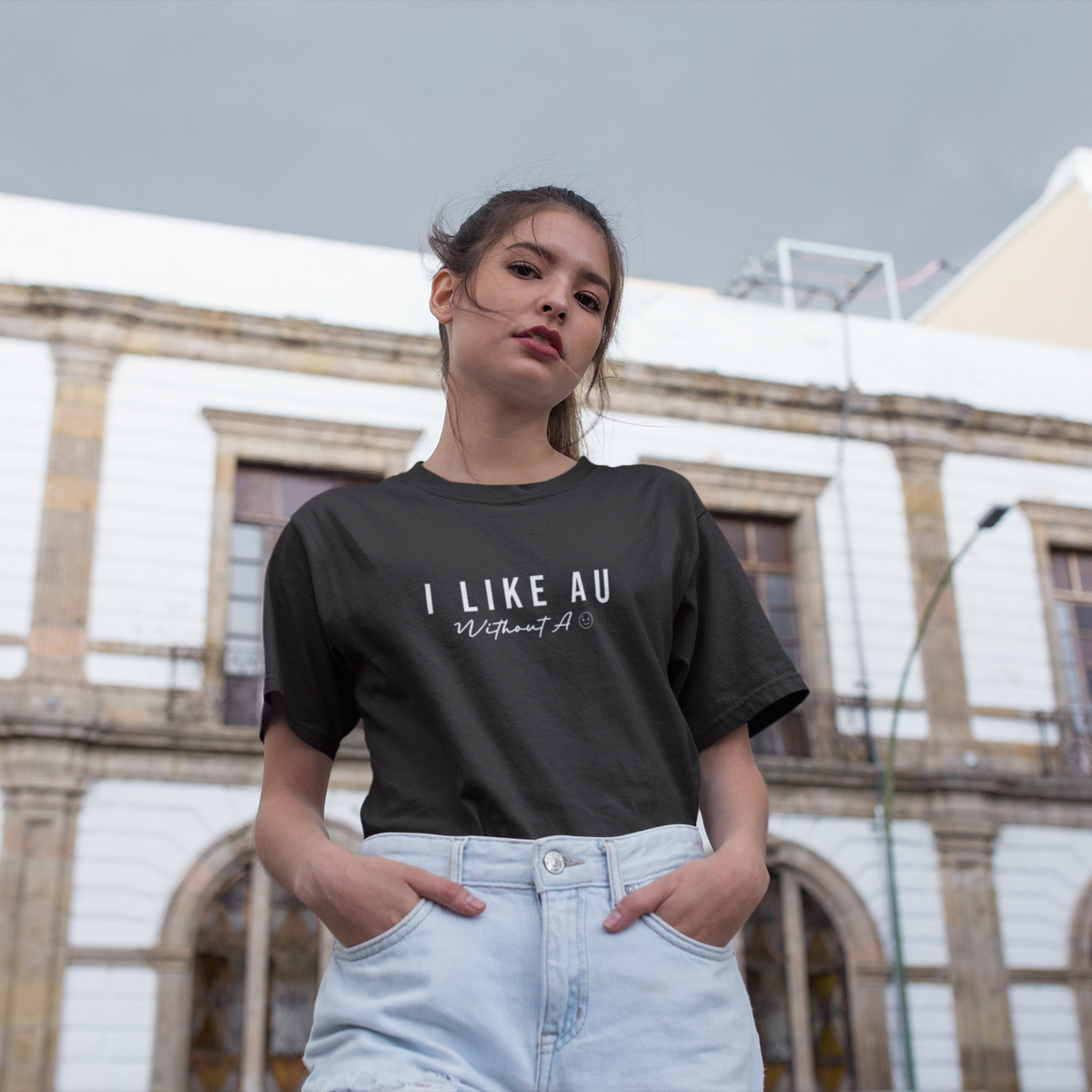 Woman wearing a black t-shirt with text, standing in front of a building.