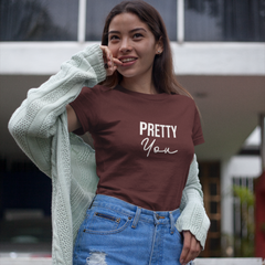 Woman wearing a brown t-shirt with 'Pretty You' text, blue shorts, and a light green cardigan.