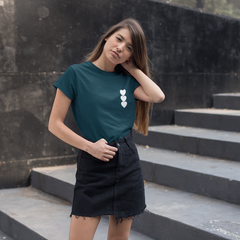 Woman in a teal shirt and black skirt standing on stone steps against a dark wall.