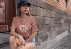 Woman wearing a pink t-shirt with text and a peace symbol, sitting against a brick wall.