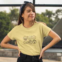 Woman wearing a light yellow t-shirt with emoji designs outdoors.