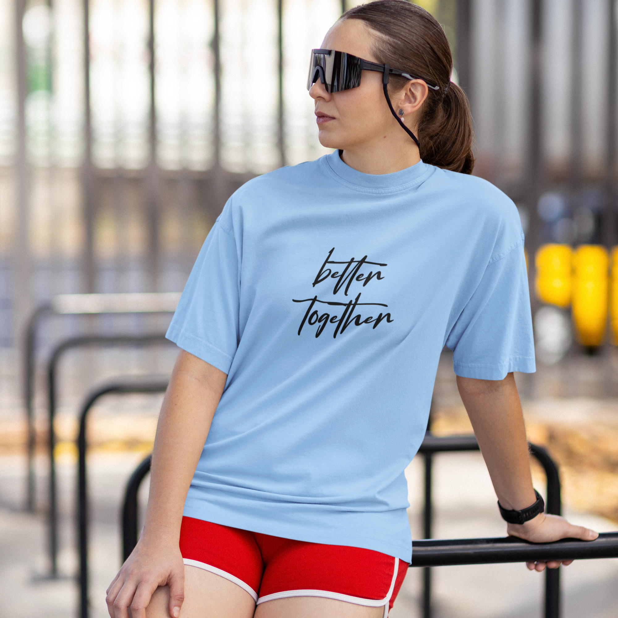 Woman wearing a light blue t-shirt with 'better together' text and red shorts, standing outdoors.