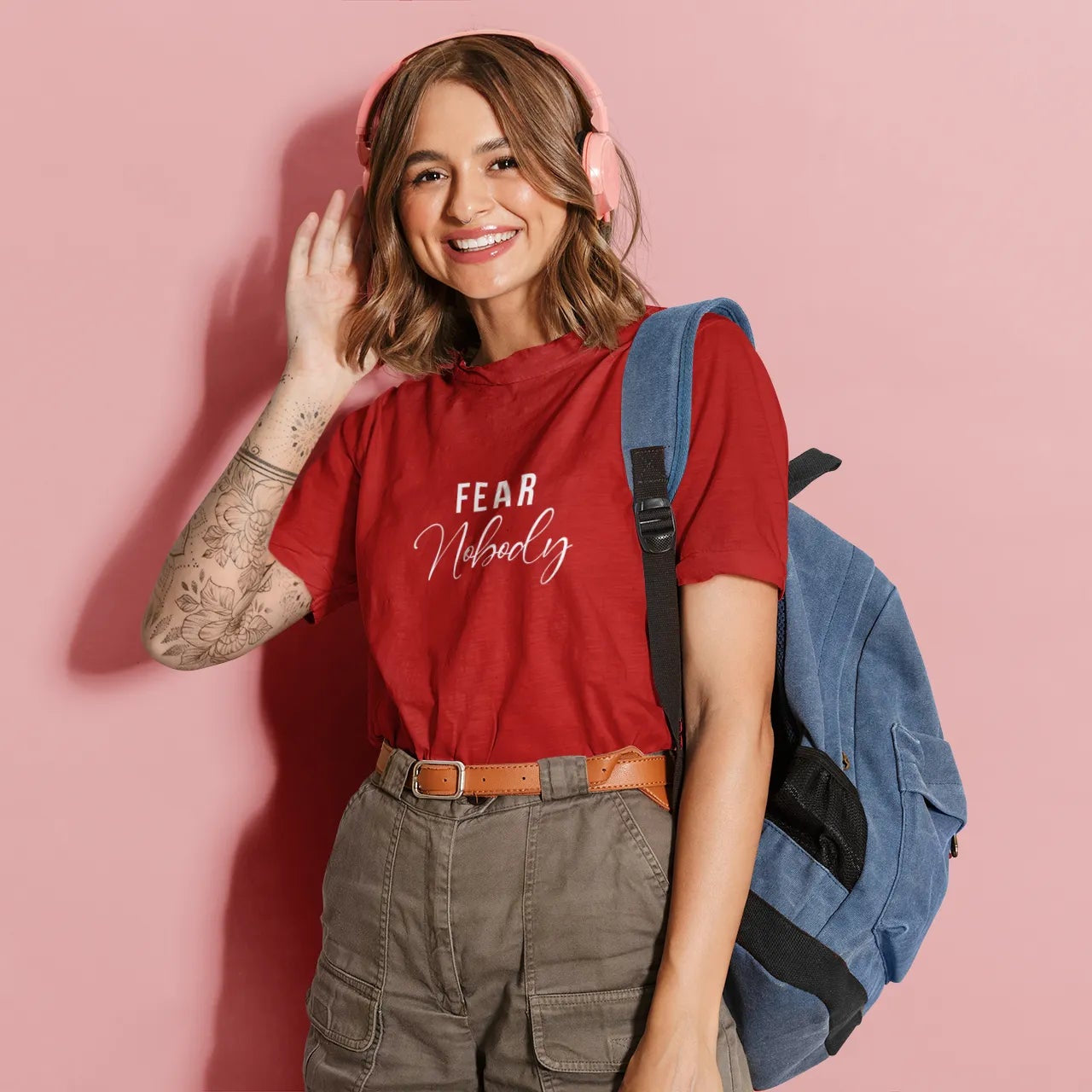 Woman wearing a red t-shirt with text, standing against a pink background