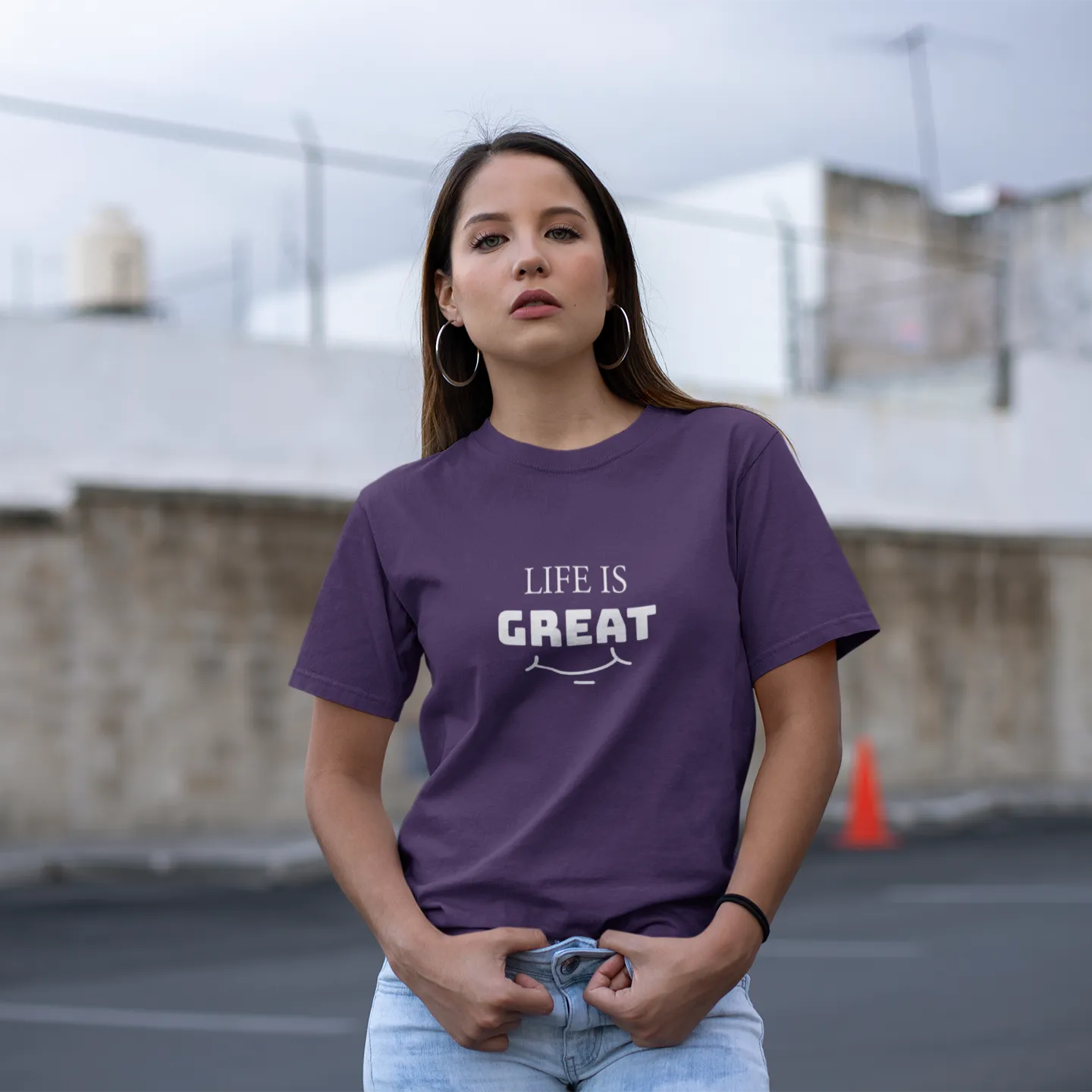 Woman wearing a purple t-shirt with 'LIFE IS GREAT' text in an outdoor setting.