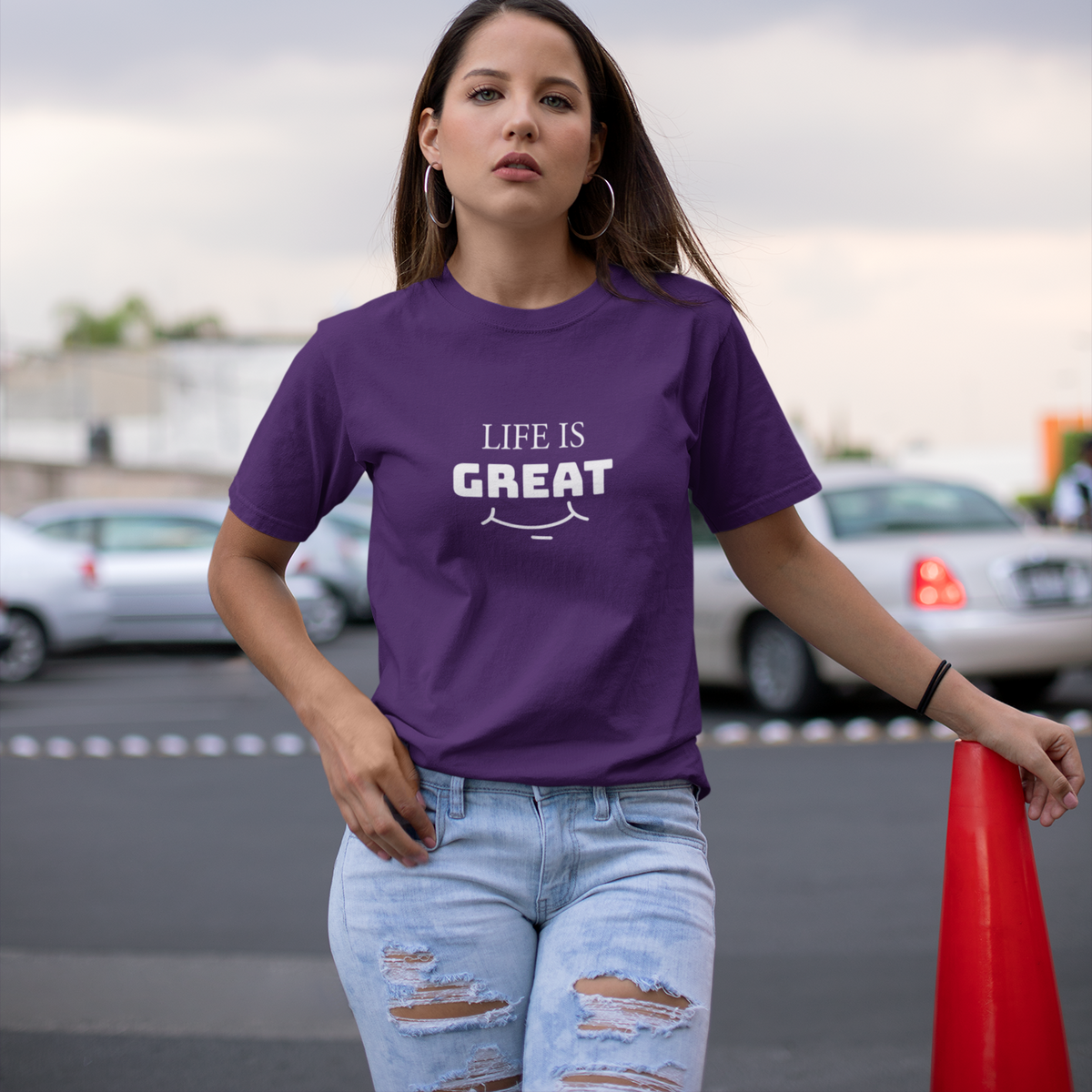 Woman wearing a purple t-shirt with 'LIFE IS GREAT' text, standing outdoors.