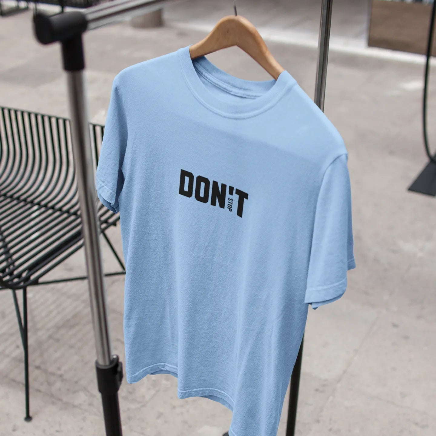 Light blue t-shirt with 'DON'T' text on a hanger against a blurred indoor background