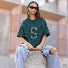 Person wearing a green t-shirt and ripped jeans sitting on a concrete block outdoors.