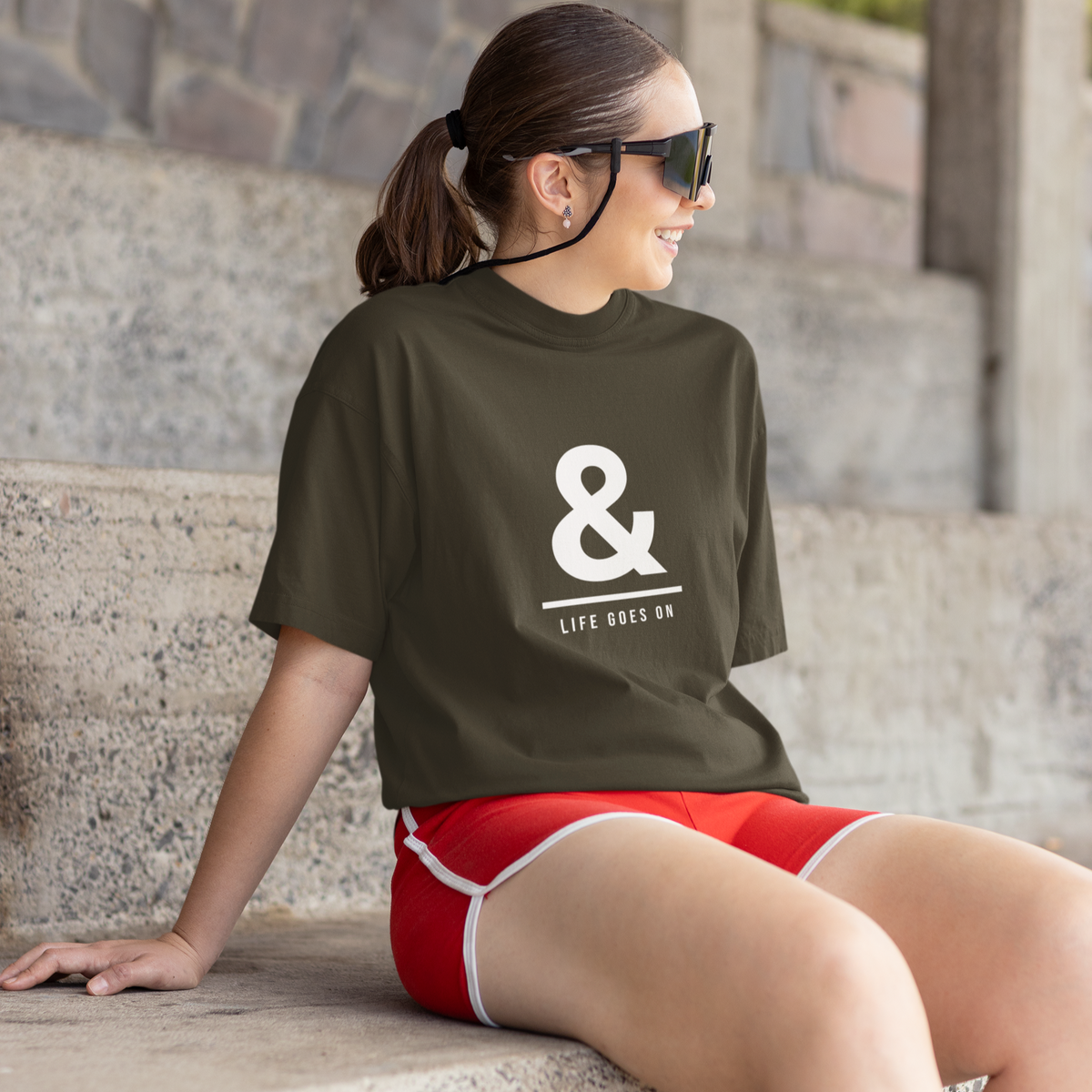 Woman wearing a green t-shirt with a white logo and red shorts sitting on stone steps.