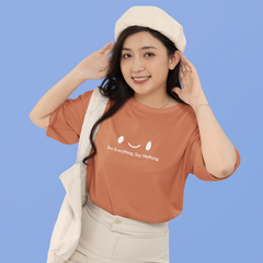 Woman wearing a brown t-shirt with text and a beige hat against a blue background