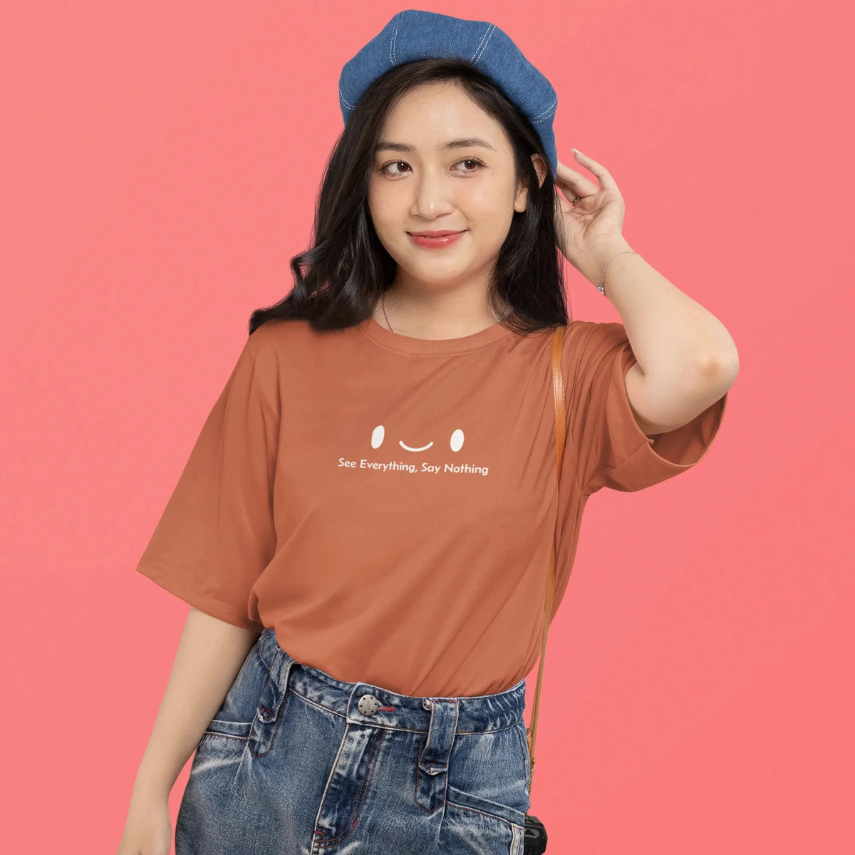 Woman wearing a brown t-shirt with text and blue jeans against a pink background