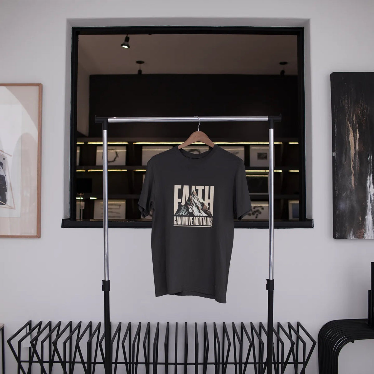 Black t-shirt with graphic design hanging on a rack in a modern interior setting.