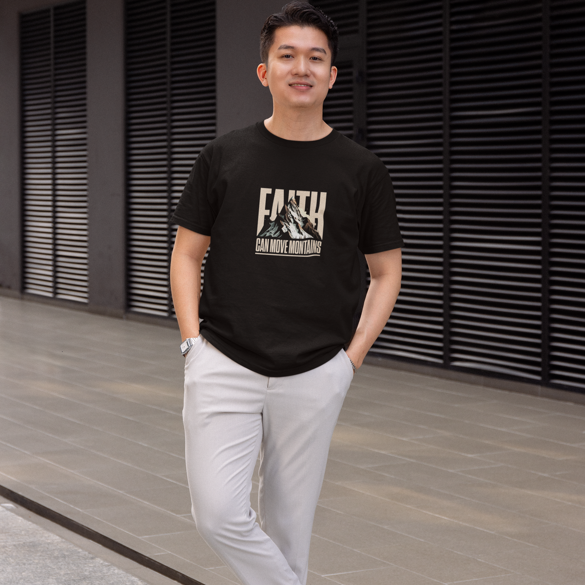 Man wearing a black t-shirt with a graphic design and text, standing in front of a modern building.