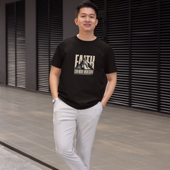 Man wearing a black t-shirt with a graphic design and text, standing in front of a modern building.