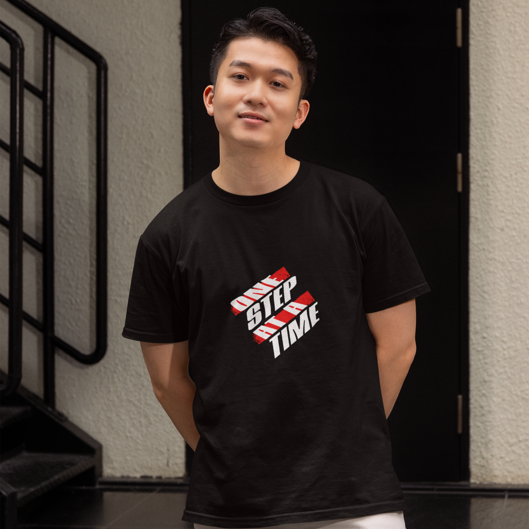 Person wearing a black t-shirt with a graphic design standing in front of a building entrance.