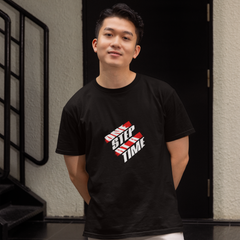 Person wearing a black t-shirt with a graphic design standing in front of a building entrance.