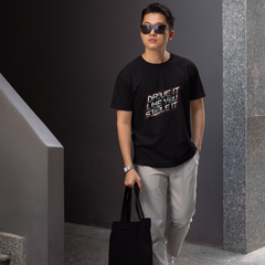 Man wearing a black t-shirt with text, holding a black bag, and standing in an indoor setting.