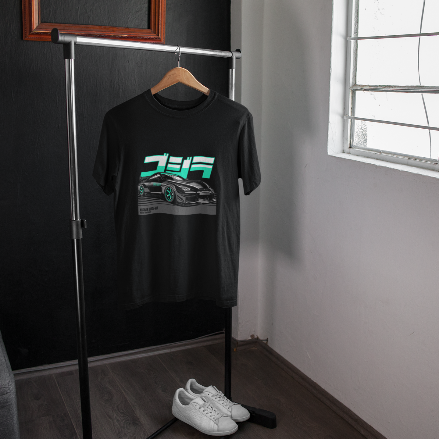 Black t-shirt with graphic design on a hanger in a room with a window.