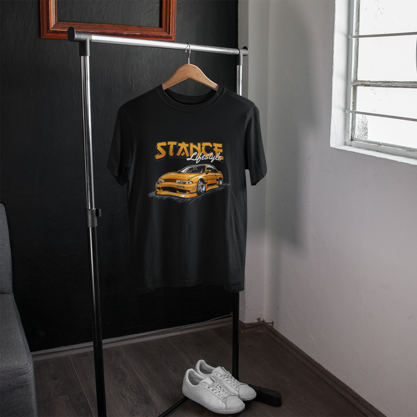 Black t-shirt with car graphic and 'STANCE' text on a hanger in a room.