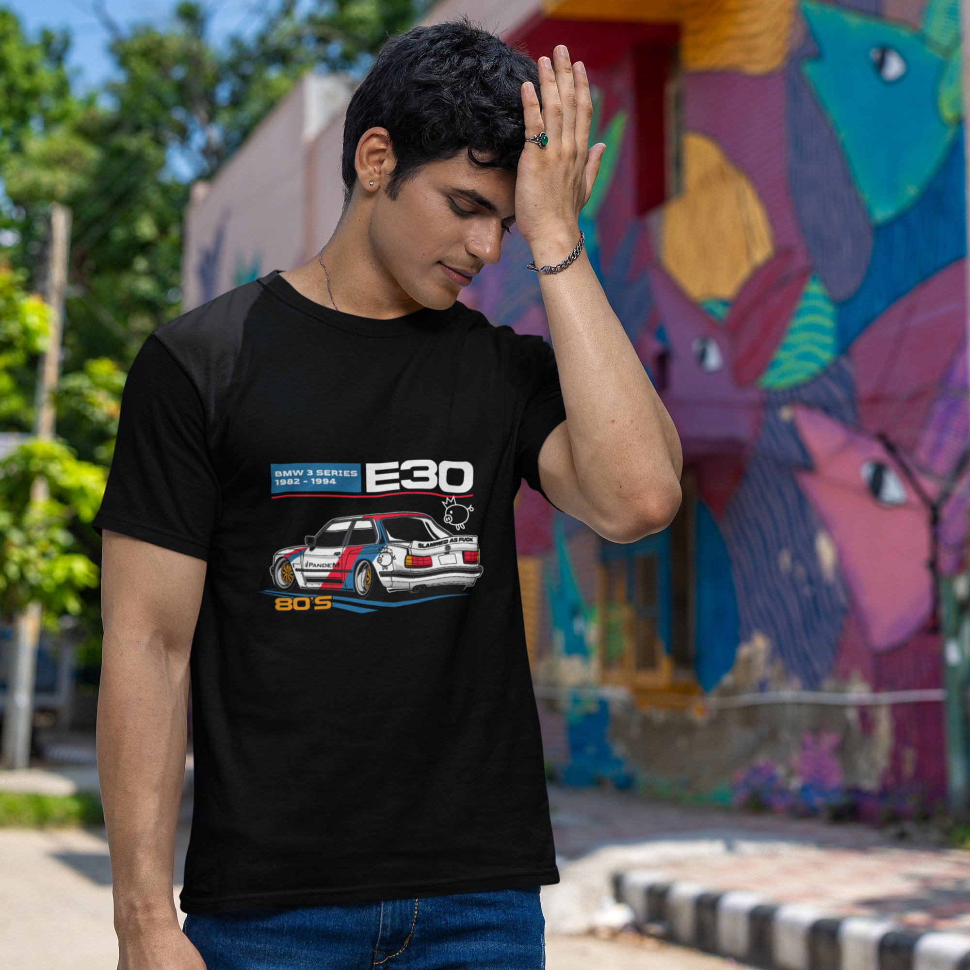 Person wearing a black t-shirt with a car design in front of a colorful mural.