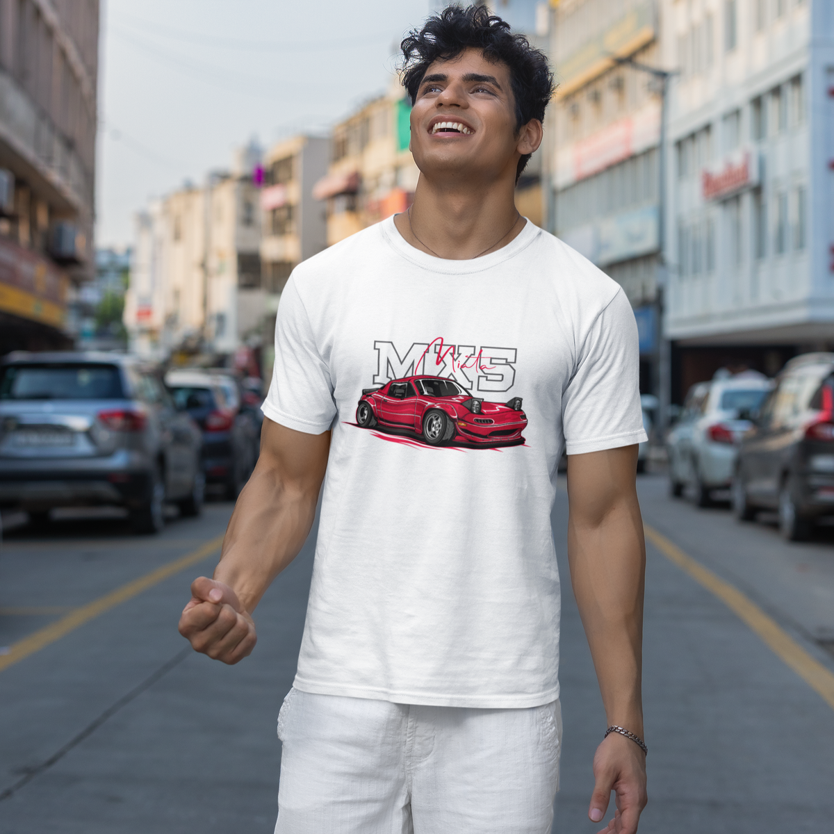 Man wearing a white t-shirt with a red car graphic and 'MKS' text on a city street.
