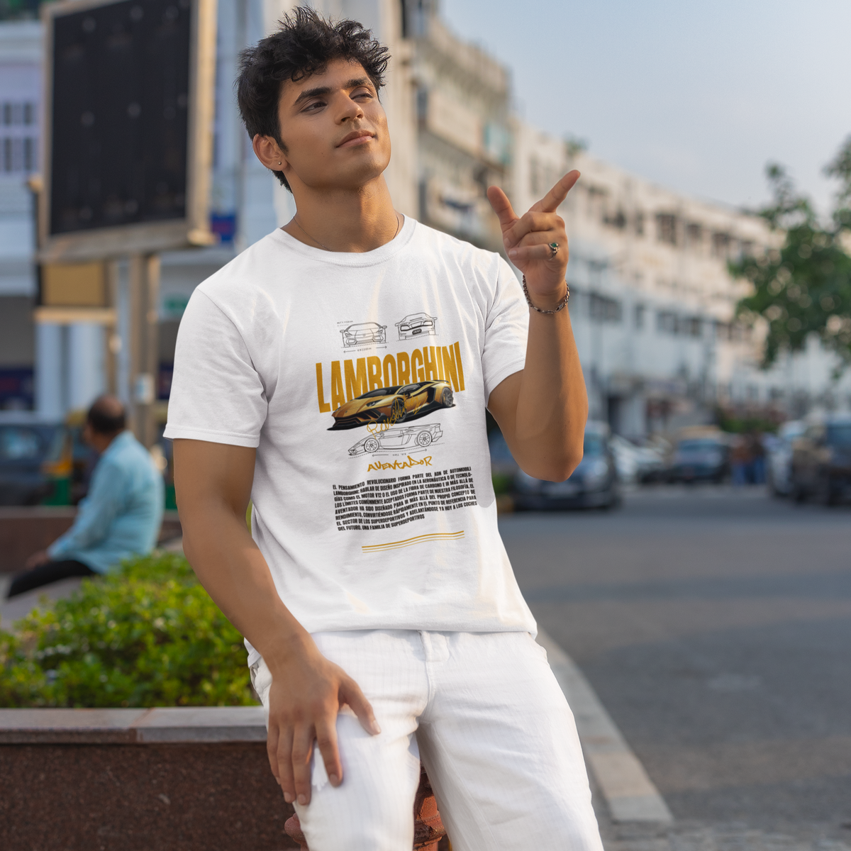 Man wearing a Lamborghini t-shirt sitting outdoors with buildings and cars in the background