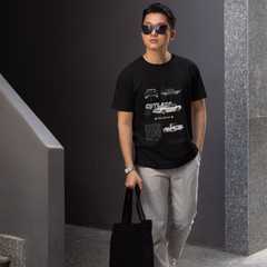 Man wearing sunglasses and a black t-shirt with graphic designs, holding a black tote bag, standing against a gray wall.