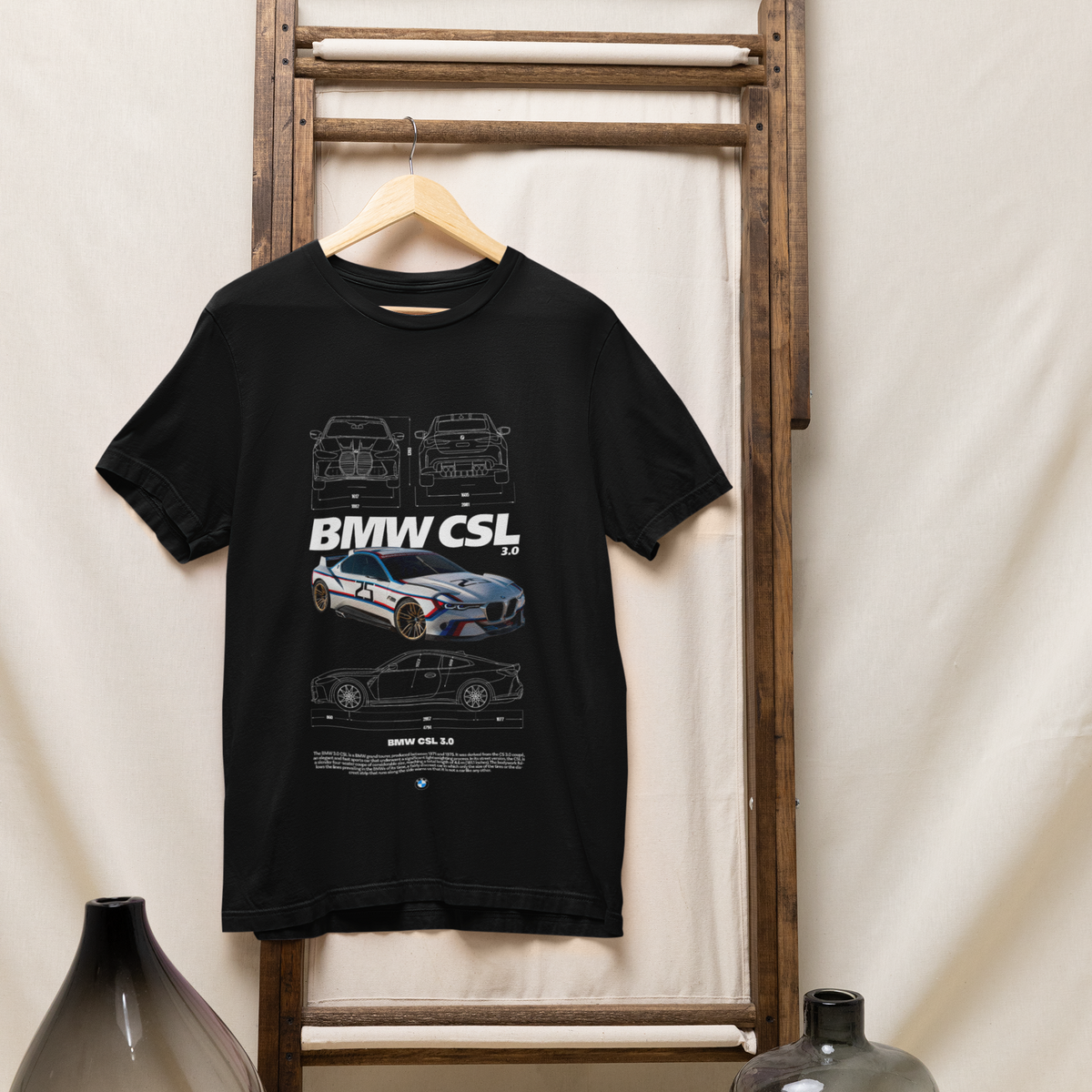 Black t-shirt with BMW CSL design hanging on a wooden rack against a white curtain background.