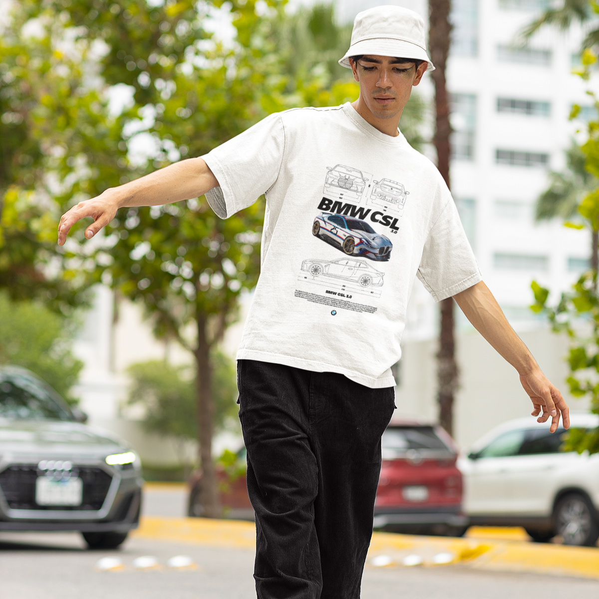 Person wearing a white t-shirt with a graphic design, black pants, and a white cap, standing on a street.