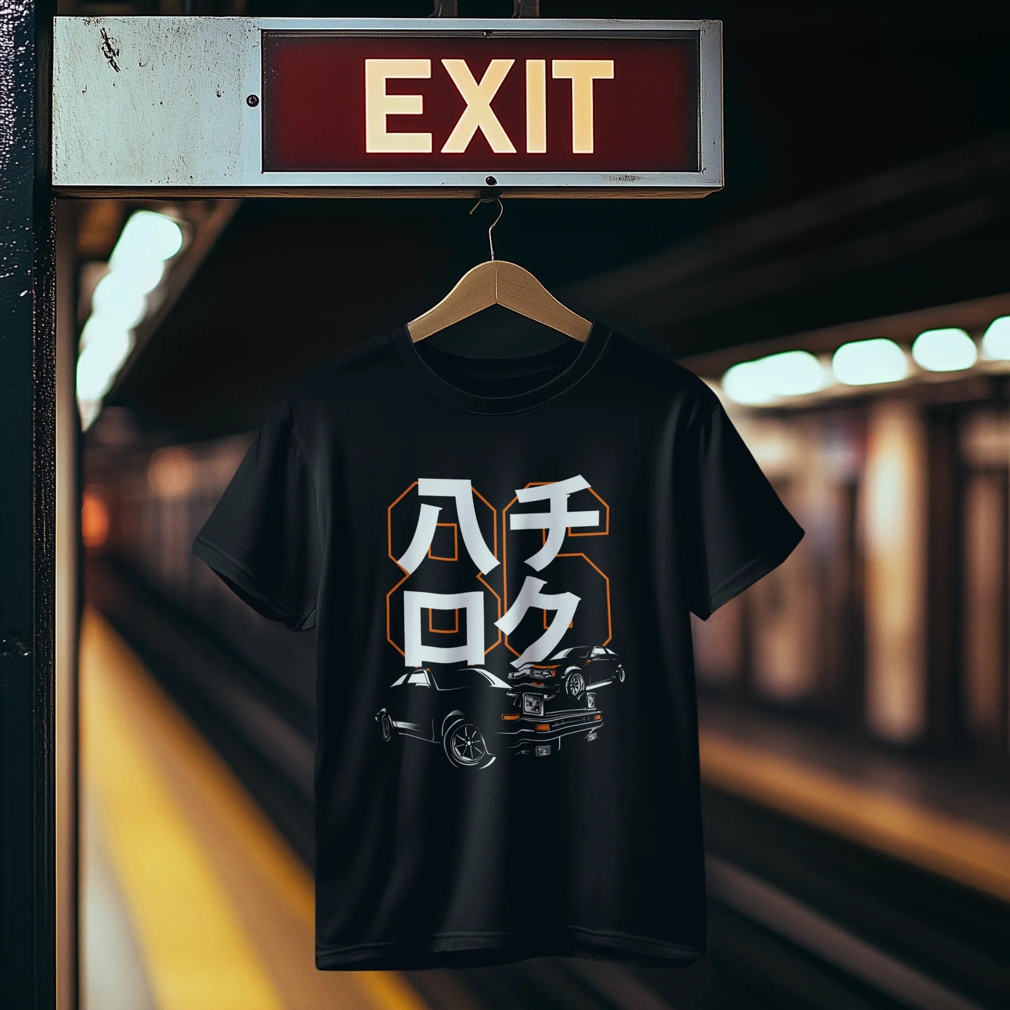 Black t-shirt with graphic design hanging on a hanger under an exit sign in a train station.
