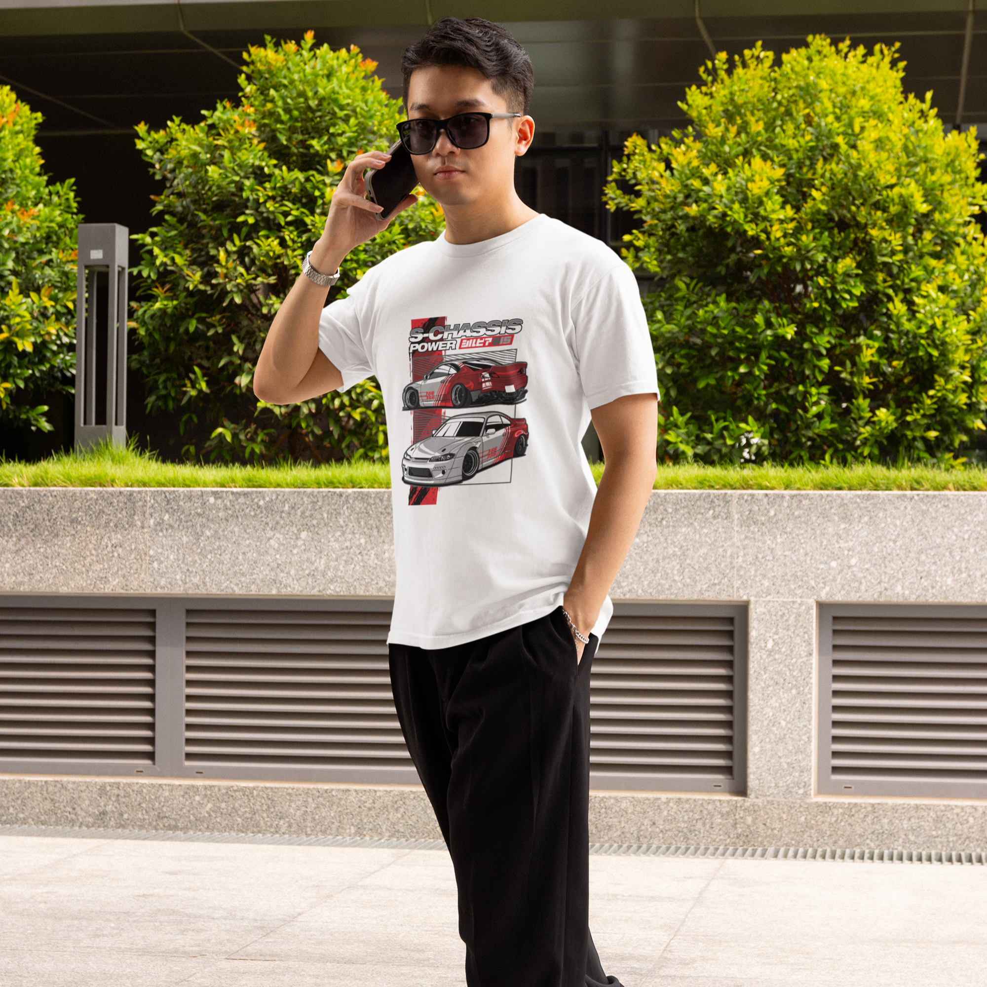 Man talking on a phone outdoors with greenery and a building in the background