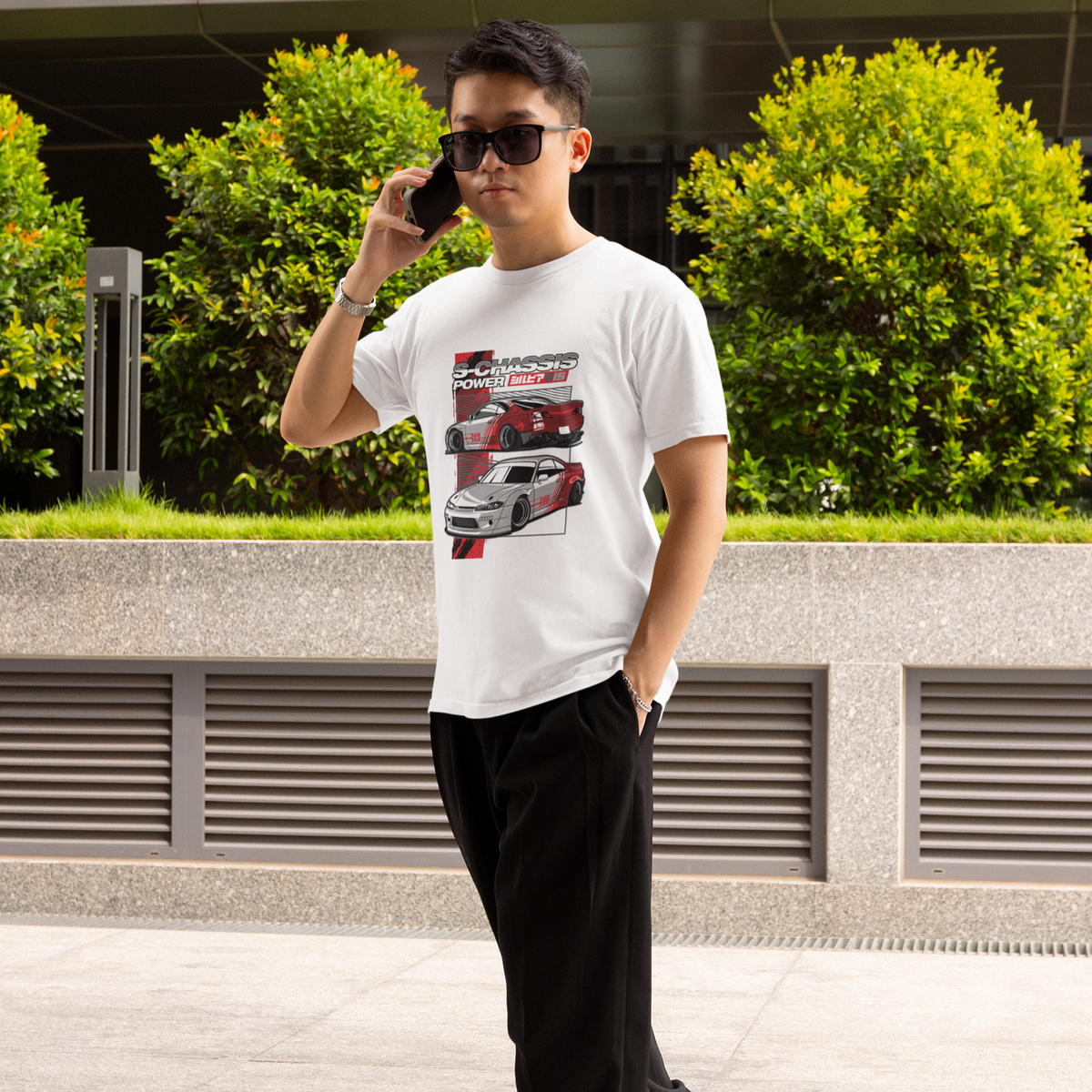 Man talking on a phone outdoors with greenery and a building in the background