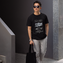 Man wearing a black t-shirt with graphics, holding a black bag, standing in a modern indoor setting.