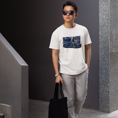Man wearing a white t-shirt with a graphic design, holding a black bag, and standing in an indoor setting.